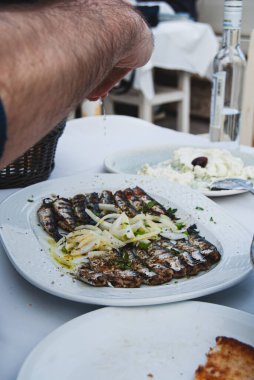 Bir tabak kızarmış balığın üzerine limon sıkan bir adam.