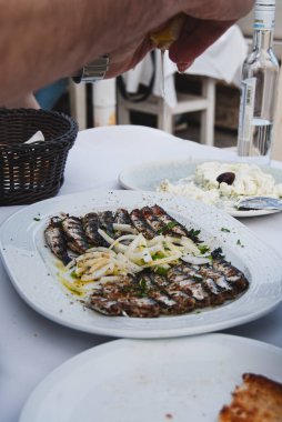 Bir tabak kızarmış balığın üzerine limon sıkan bir adam.