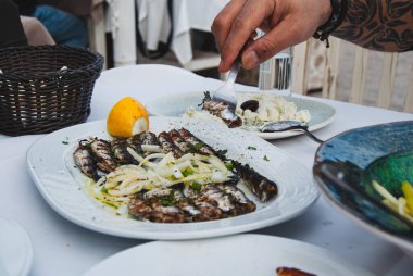 Limonlu, otlu, soğanlı, sardalyalı ızgara balık yiyen bir adamın yakın plan fotoğrafı.