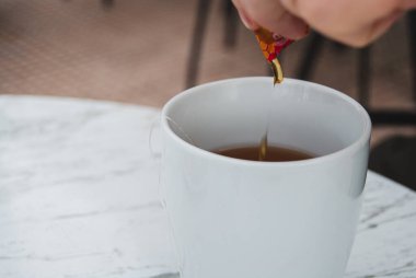 Bir fincan sıcak çaya bal dök, masaya kaşık koy, yakından çek.