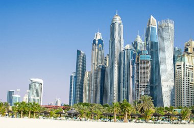 Modern metropolün gökdelenleri, sıcak ve güneşli bir günde, lüks beyaz kumlu plajın üzerinde yükselir. Dubai, Birleşik Arap Emirlikleri