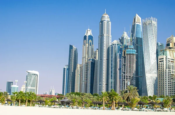 stock image The skyscrapers of the modern metropolis rise above the luxurious white sandy beach on a warm sunny day. Dubai, United Arab Emirates