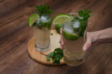 Hanımefendinin eli, ahşap arka planda limonlu bir bardak mojito tutuyor..