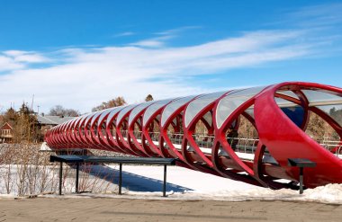 Kırmızı bir yaya köprüsü üzerinde açık mavi gökyüzü olan donmuş bir nehir boyunca uzanır. Bankalar karla kaplı ve uzak mesafeden çıplak ağaçlar görülebiliyor. Bu da soğuk bir kış günü olduğunu gösteriyor..