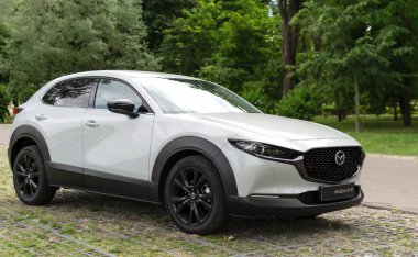 Kyiv, Ukrayna 05 / 29 / 2024 - Nehir kıyısı yakınında beyaz bir Mazda arabası, bir şehir köprüsü ve modern yüksek binaların arka planına park edilmiş durumda. Ön manzara radyatör ızgarasının zarif tasarımını ve Mazda logosunu vurguluyor.