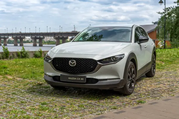 stock image Kyiv, Ukraine 05/29/2024 - A white Mazda car is parked near the riverbank, against the background of a city bridge and modern high-rise buildings. The front view emphasizes the elegant design of the radiator grille and the signature Mazda logo, refle