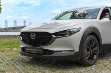 Modaya uygun beyaz kompakt Mazda 30, açık mavi bir gökyüzü altında nehir köprüsü yakınındaki kaldırım taşları üzerinde çekilmiş. 29.04 Kyiv, Ukrayna,