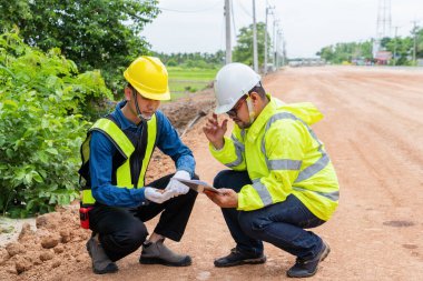 Mühendis ve ustabaşı asfalt dökmeden önce yol yapım toprağını inceliyor.