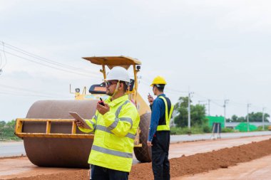 Asyalı bir mühendis telsiz kullanarak yol silindirini inceliyor..