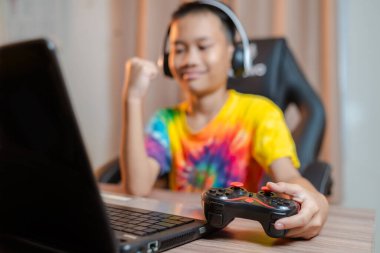 Mutlu Asyalı çocuk boş zamanlarında online bir bilgisayar oyunu kazandıktan sonra ellerini kaldırıyor. joystickle joystick 'e odaklan