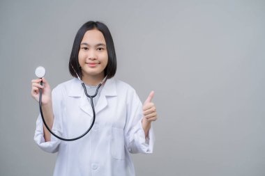 Asyalı genç kız izole edilmiş, doktor üniforması giyiyor ve elinde tıbbi bir steteskop tutuyor..