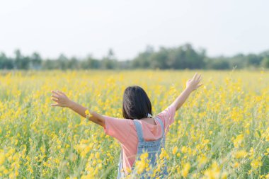 Genç Asyalı kız sarı çiçeklerle dolu bir arazide mutlu mesut oynuyor.