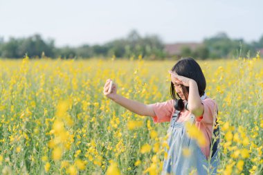 Genç Asyalı kız sarı çiçeklerle dolu bir arazide mutlu mesut oynuyor.