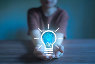 Işıldayan ampulle ve insan beyniyle kadın elinin yakın çekimi.