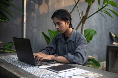 Kafede masa başında oturmuş dizüstü bilgisayar ve kitaplar üzerinde çalışan Asyalı genç adam.