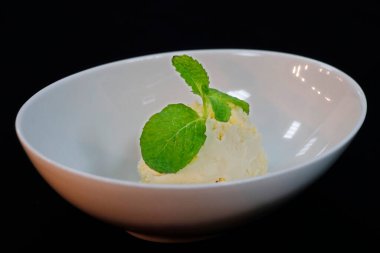 Vanila dondurma kepçesi, içinde nane yaprağı olan bir kase, siyah arkaplan.