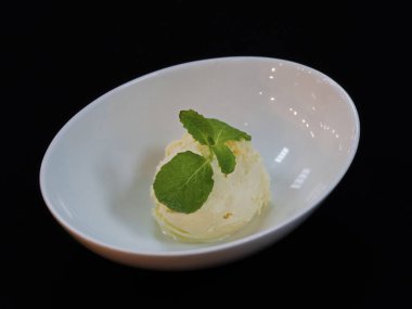 Vanila dondurma kepçesi, içinde nane yaprağı olan bir kase, siyah arkaplan.