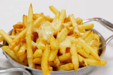 Erimiş peynirli patates kızartması, beyaz arka planlı metal bir kasede.
