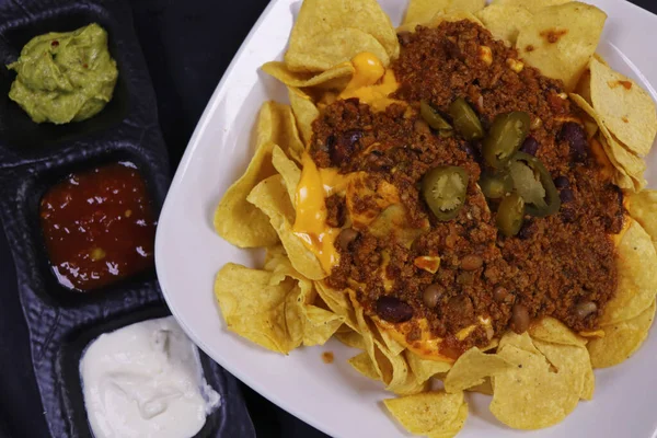 Geleneksel Meksika atıştırmalığı, mısır tortilla cipsi ve avokado guacamole, chili con carne, salsa ve ekşi krema. Nachos olarak bilinir.