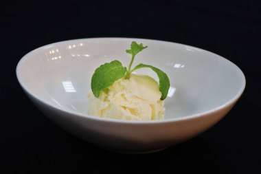 Vanila dondurma kepçesi, içinde nane yaprağı olan bir kase, siyah arkaplan.