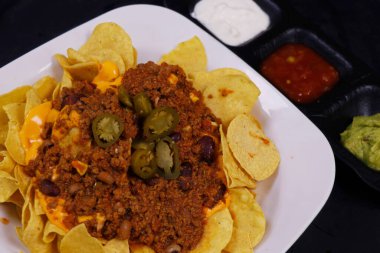 Geleneksel Meksika atıştırmalığı, mısır tortilla cipsi ve avokado guacamole, chili con carne, salsa ve ekşi krema. Nachos olarak bilinir.