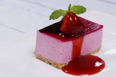 Beyaz tabakta ahududu soslu çilekli kek.