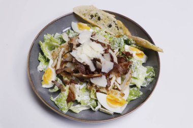 Tavuk, domuz pastırması, kızarmış ekmek, peynir ve marullu klasik sezar salatası.