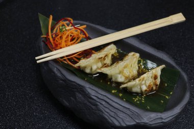 Asya usulü hamur yemeği, tavuk ve karides. Siyah arka planda soya sosuyla doldurulmuş gyoza.