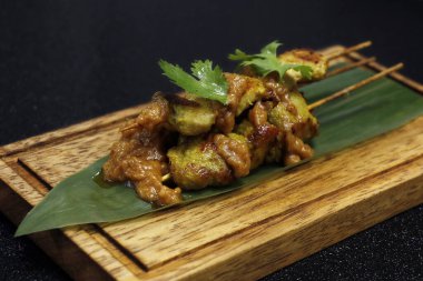 Keskin fıstık soslu, siyah arka planlı bambu yapraklı Endonezya usulü tavuk şişi.