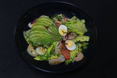 Avokado salatası, karides ve bıldırcın yumurtası siyah arka planda.