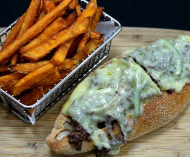 Philly cheese steak sandwich and fries on a wood board. clipart