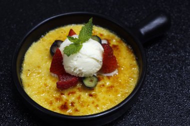 crema catalana veya creme brulee dondurmalı ve siyah arkaplanlı taze böğürtlen