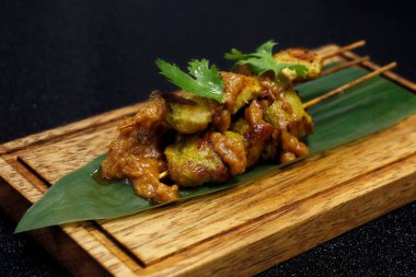 Keskin fıstık soslu, siyah arka planlı bambu yapraklı Endonezya usulü tavuk şişi.