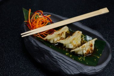 Asya usulü hamur yemeği, tavuk ve karides. Siyah arka planda soya sosuyla doldurulmuş gyoza.