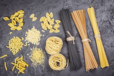 Makarna ayı. Siyah taş zemin üzerinde pişmemiş makarna ve erişte çeşitleri, metin için fotokopi alanı ile üst görünüm. İtalyan mutfağı konsepti. Yemek masasında farklı ham makarna koleksiyonu