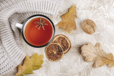 Sonbahar içkisi, diş minesi bardağında sıcak çay. Kuru yapraklar, fındıklar, örgü süveter ve baharatlarla sonbahar arka planı