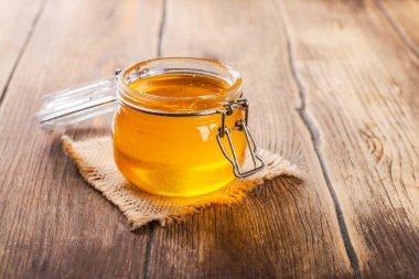 Kırsal ahşap masada çiçekli, ballı cam kavanoz.