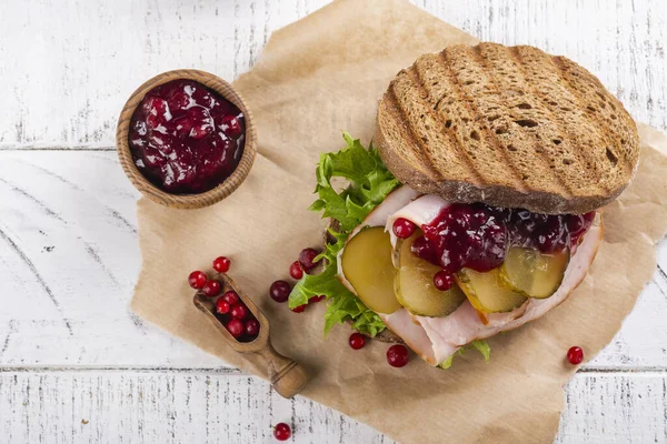Homemade leftover thanksgiving day sandwich with turkey, cranberry sauce and vegetables. White wooden background