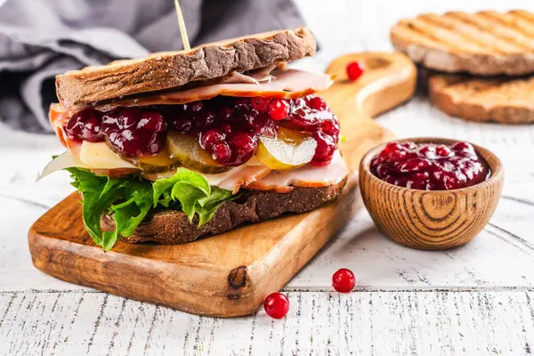 Homemade leftover thanksgiving day sandwich with turkey, cranberry sauce and vegetables. White wooden background