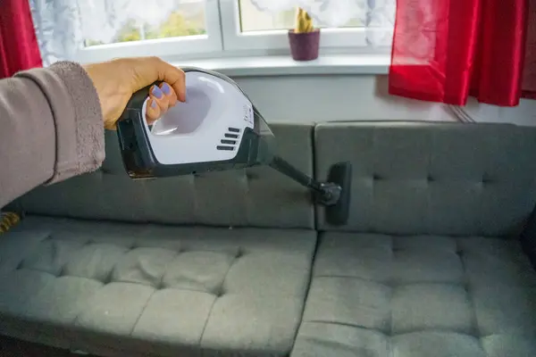Woman with handheld vacuum cleaning on sofa. High quality photo