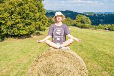 Saman 'ın yanında ekmekler içinde meditasyon yapan kız. Hayvan yemi için saman. Çiftçilik. Kış için kuru saman stokları. Yüksek kalite fotoğraf