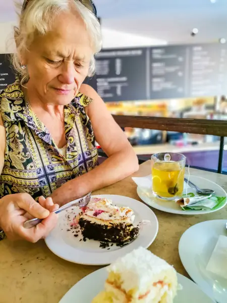 Old lady wearing jewelry having tea with sweet cake at a restaurant. High quality photo