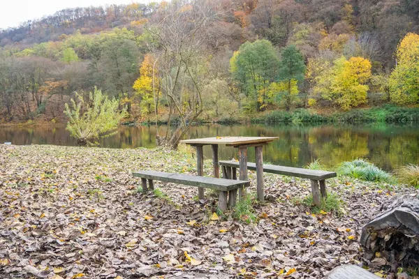 Picnic wooden benches and table by the river Berunka in autumn season, place to relax with forest and mountains. High quality photo
