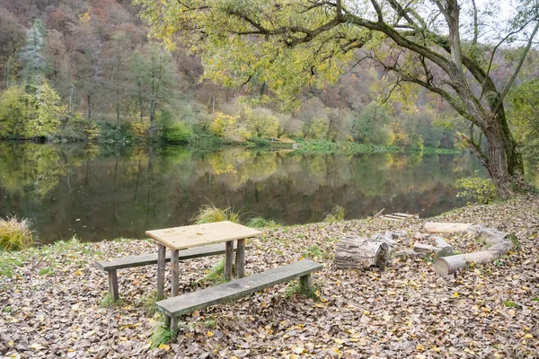 Picnic wooden benches and table by the river Berunka in autumn season, place to relax with a tree. High quality photo