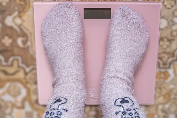 A woman in fun socks weighing himself on a electronic floor scale, top view. Weight control concept. High quality photo
