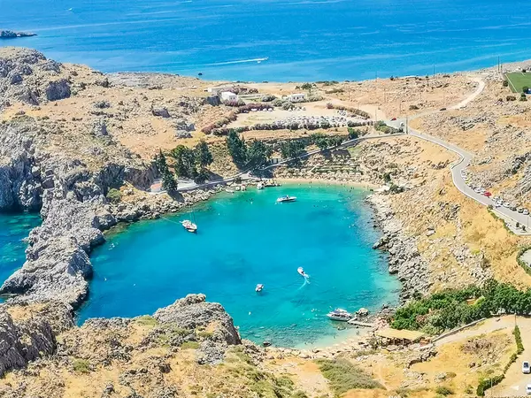 View of St. Pauls Bay in Lindos. Rocks surround the sea in the shape of a heart. Near the bay are the white houses of the village. Mountain ranges and the open sea on the horizon. High quality photo