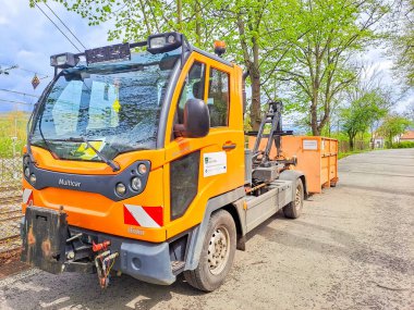 Prag - Çek - 10 Nisan 2024 Atık Yönetim Teması. Turuncu bir çöp toplayıcı yolun kenarında duruyor. Yeşillik ve dallar için. Yüksek kalite fotoğraf