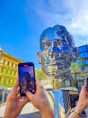 Prague- Czech- 12 april 2024: Statue of Franz Kafka, the latest work by artist David Cerny is located at yard of the shopping center Quadrio. Tourists film on their phones how the statue spins  clipart
