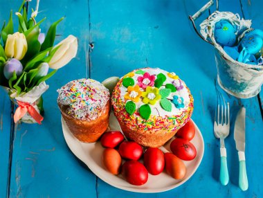 Paskalya pastası, renkli yumurtalar ve açık mavi masada çiçekler, yazı için yer. Yüksek kalite fotoğraf