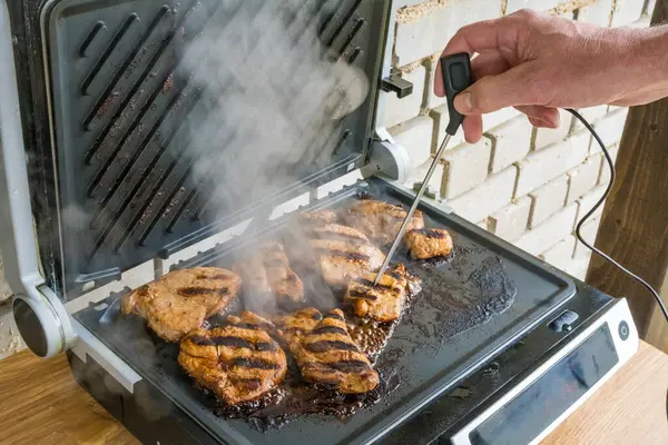 Sıcaklığı ölçerek bifteğin hazır olup olmadığını kontrol ediyorum. Elektrikli ızgarada pişirilmiş etli biftek. Izgara, barbekü konsepti. Ahşap arka planda oruç tutmanın sonu. Yiyecek ve mutfak konsepti.